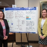 Two student presenters smiling and posing for a photo with their shared poster